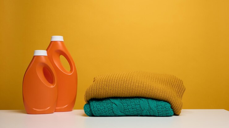 اطلاع از قیمت مایع لباسشویی مخصوص شستشو با دست کیفیت جهانی 1 stack washed folded clothes plastic orange large bottle with liquid detergent stand white table yellow background routine homework 116441 21726